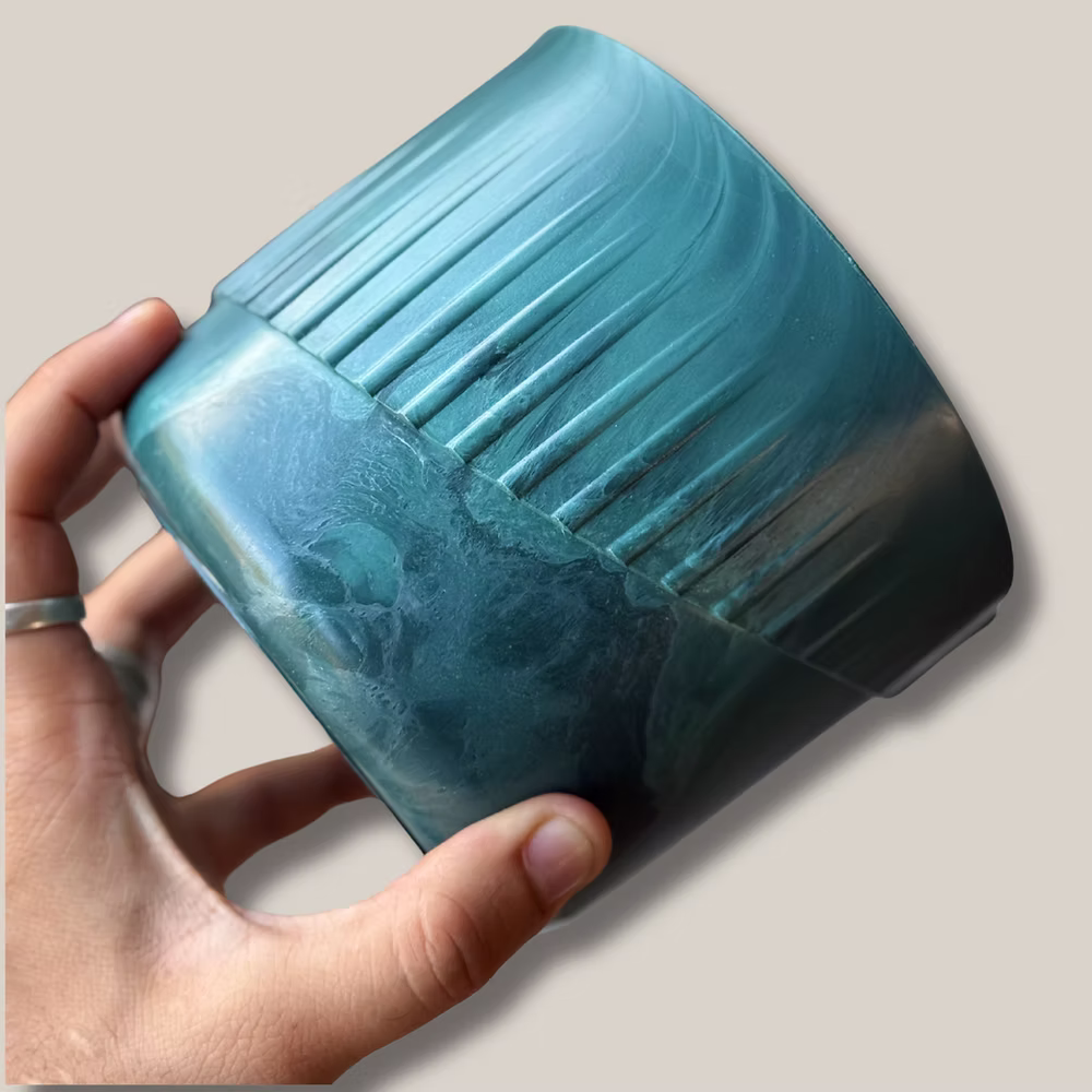 Handmade recycled ocean plastic plant pot catching light, showing swirls of green and blue from repurposed fishing nets.