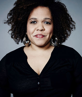 Light-skinned woman of color, wearing pants and a black shirt, with silver earrings.