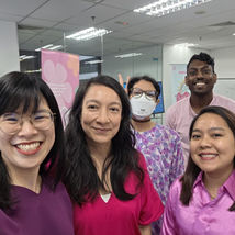 Five people smiling in an office, one wearing a mask