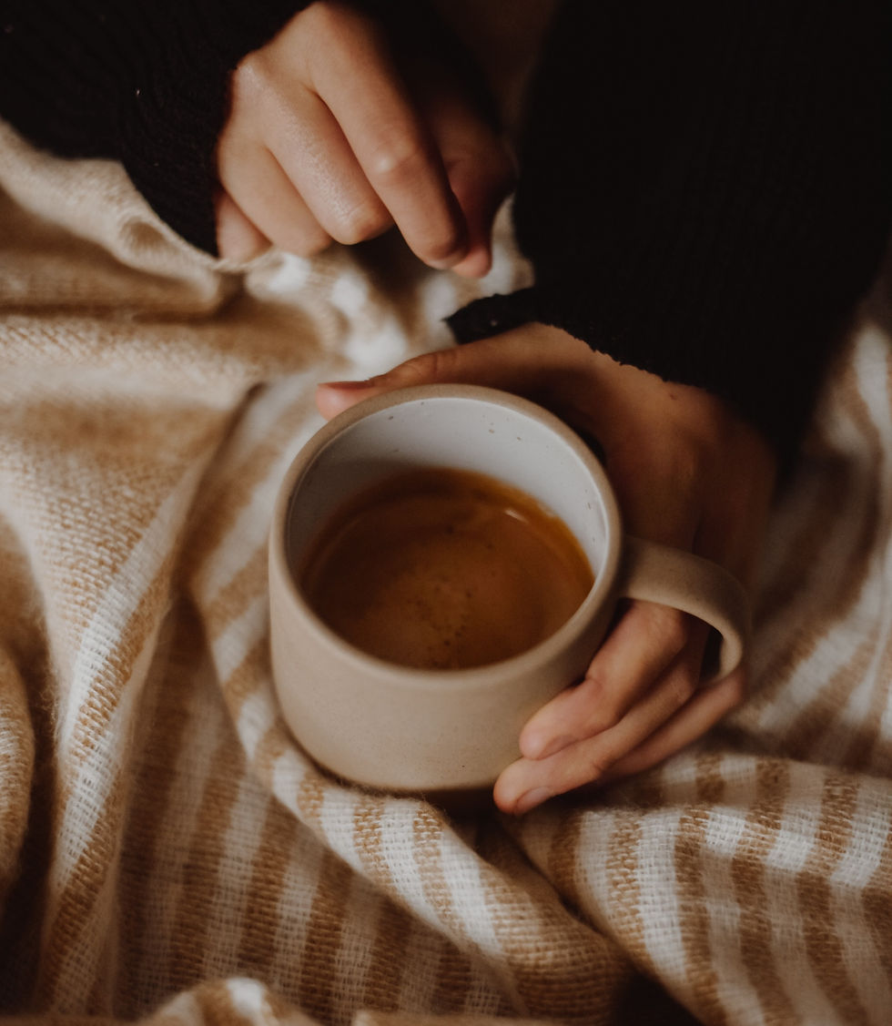Lady sat with a blanket and a cup of coffee in her hand.