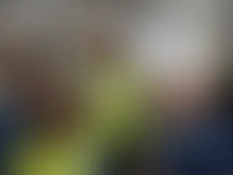 Female plant manager wearing a hard hat and high-visibility vest leading a diverse team discussion on a packaging production floor, referencing performance priorities on a whiteboard beside an active conveyor line.