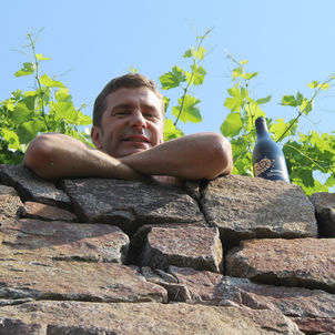 Winzer lehnt an Steinmauer, Wein neben ihm eine Flasche Wein
