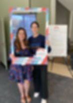 Two women smiling, holding a colorful frame reading "GlobalSkin Conference 2025 Champion" with a conference poster in the background.