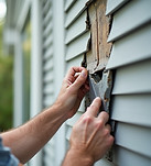 A contractor repairs vinyl siding.