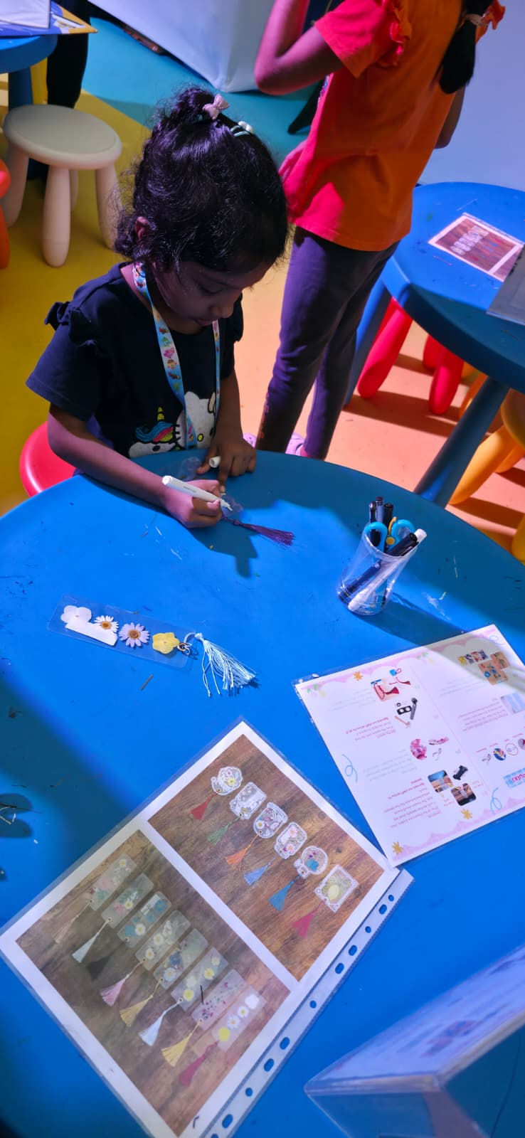 Emcee Singapore - A girl making a floral bookmark based on the sample design.