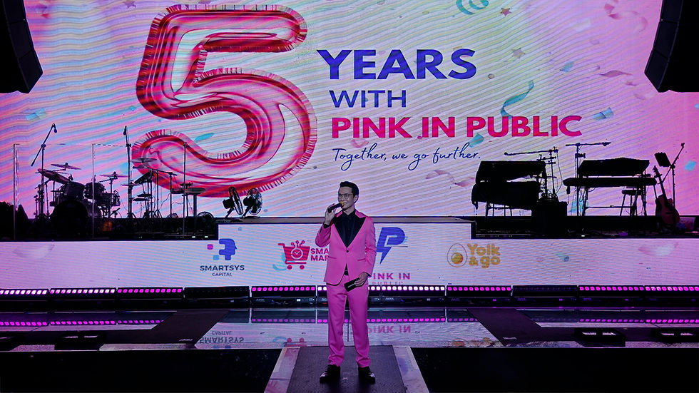 Emcee Singapore - Emcee Ivan dressed in a vibrant pink suit stands on stage addressing the guests, celebrating the "5 Years with Pink in Public" event.