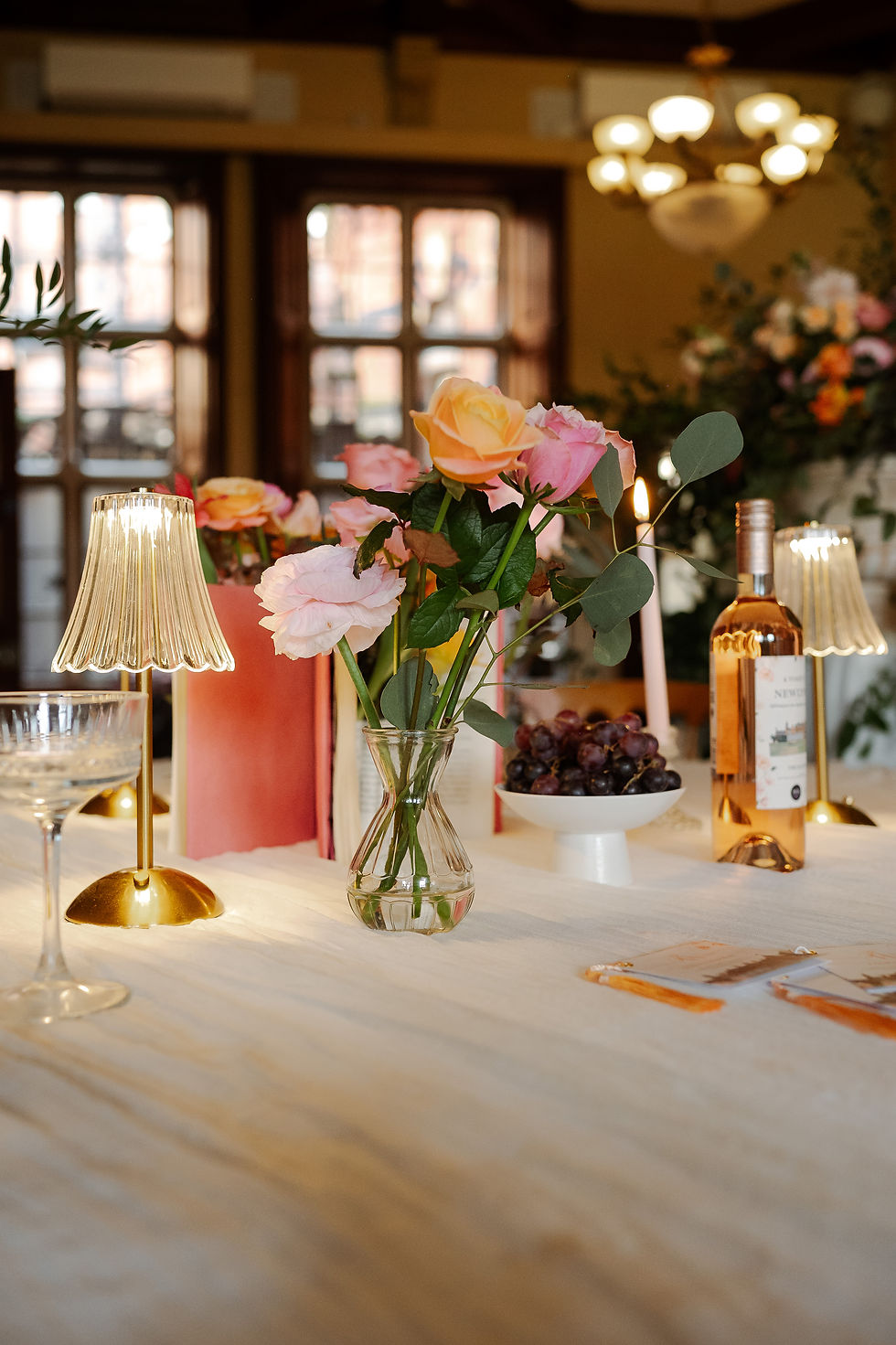 Elegant table setting at the Elvetham Hotel with pink and peach roses, gold lamps, wine, and grapes in a warm softly lit room