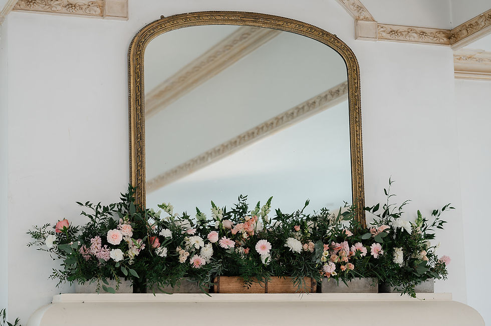 Ornate gold mirror above a lush pastel floral arrangement on a white mantel at Northbrook park, with white walls and decorative molding.