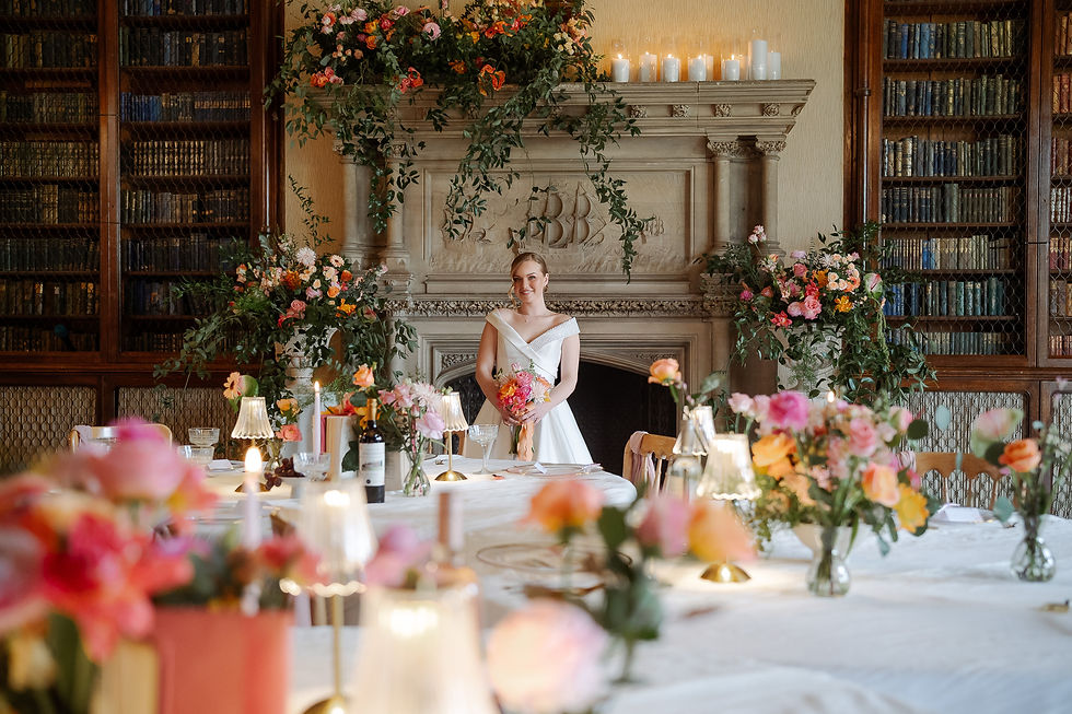 Smiling bride in white dress holds bouquet in a candlelit, flower-filled library dining room with bookshelves and fireplace at the Elevtham Hotel, Hampshire