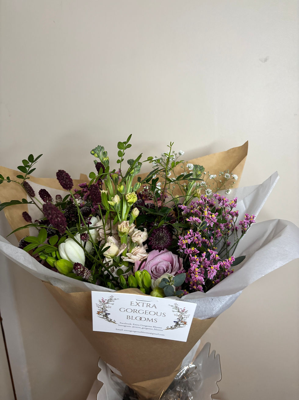 Mixed bouquet of purple, pink, white and green flowers wrapped in brown paper, with card reading EXTRA GORGEOUS BLOOMS.