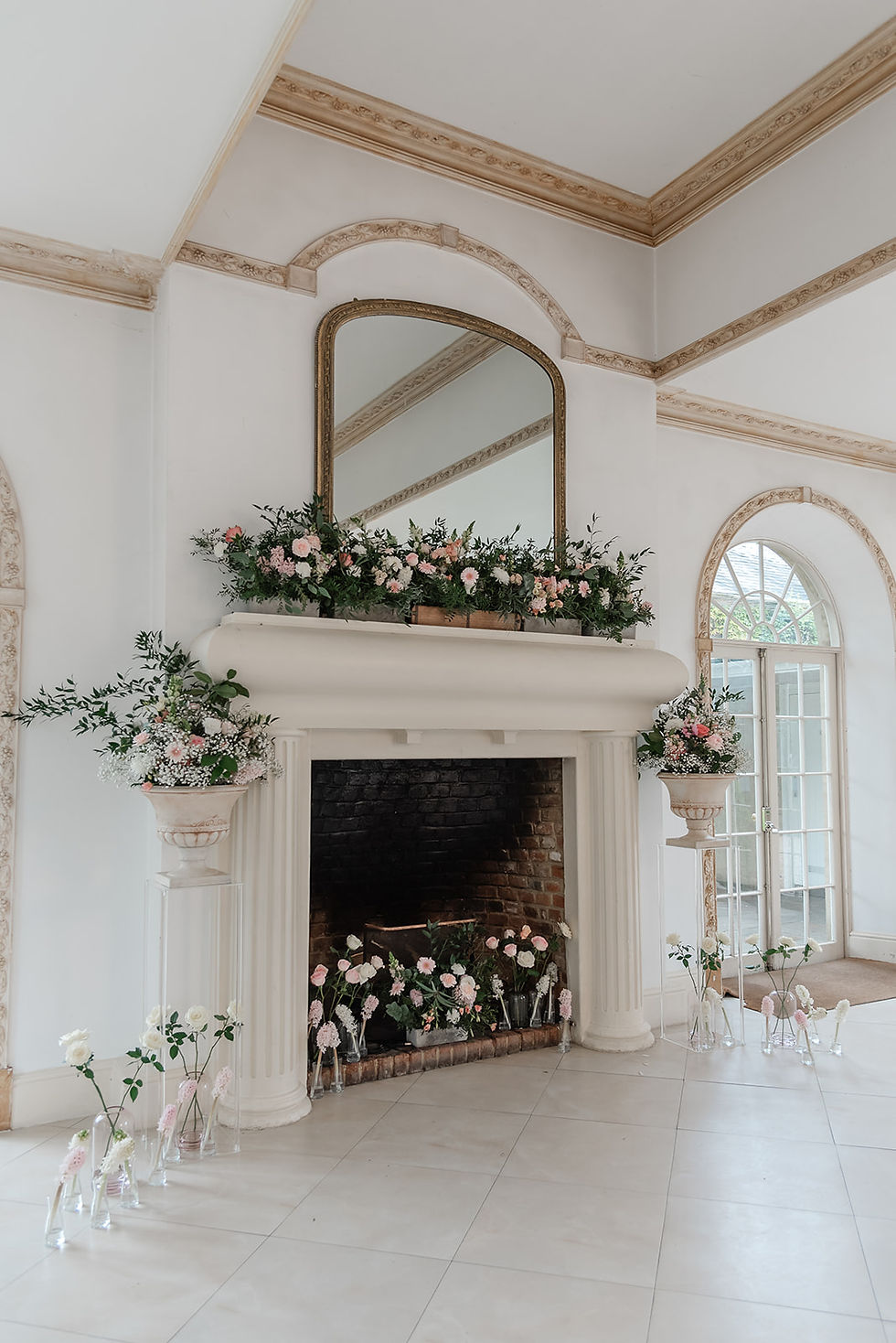Elegant vine room at Northbrook Park, Hampshire with a floral-decorated fireplace, tall mirror, and arched doors, styled for a soft romantic event