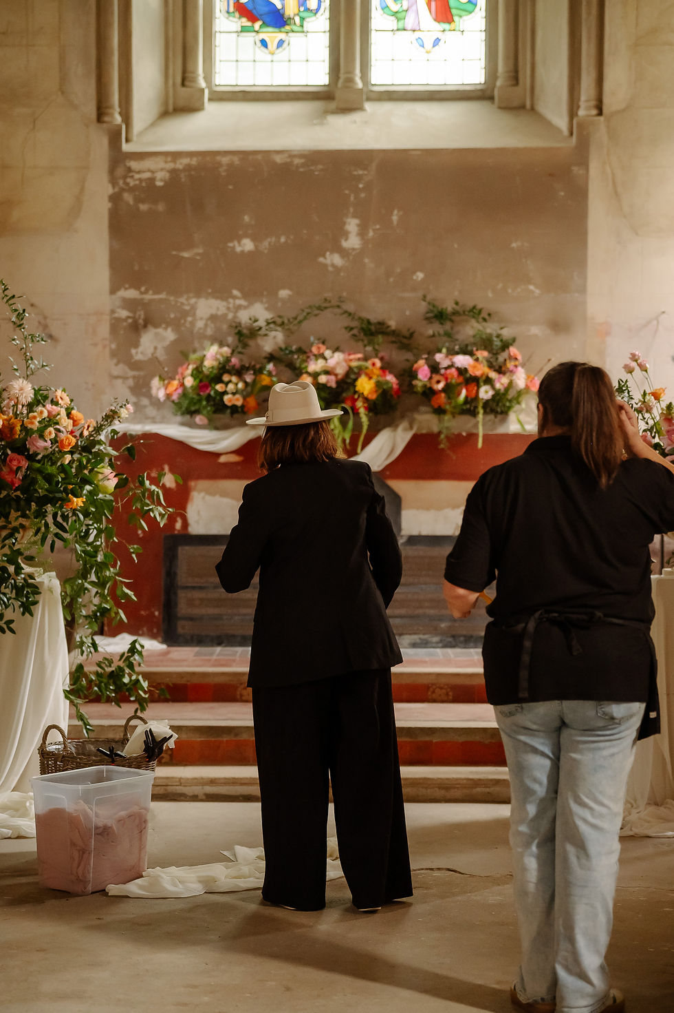 Two people stand in a flower-filled bell tower at the elvetham hotel, hook before an altar, with stained glass above and a calm, reverent mood.