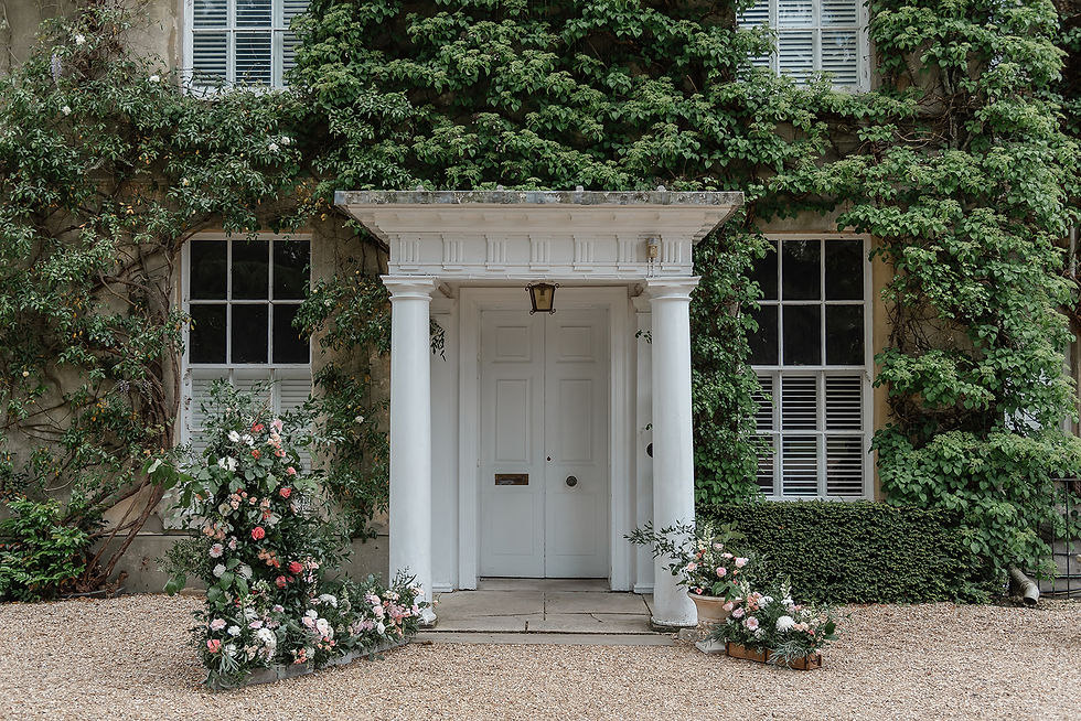 White columned front door at northbrook park on ivy-covered house, framed by pink and white flowers over a gravel path.