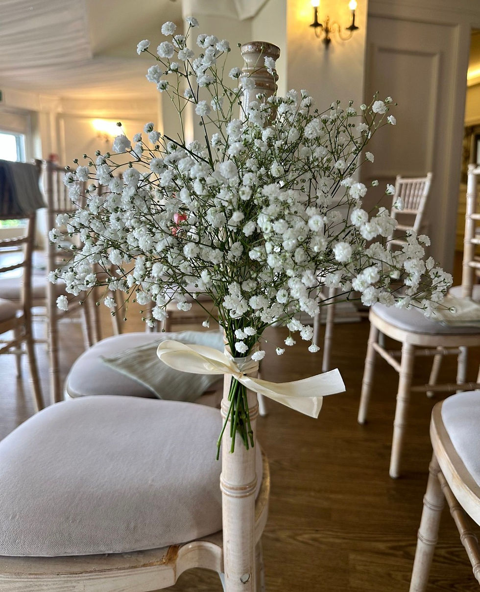 White baby's breath bouquet tied with a cream ribbon on a chair in a warm, elegant room with white chairs and wood floor
