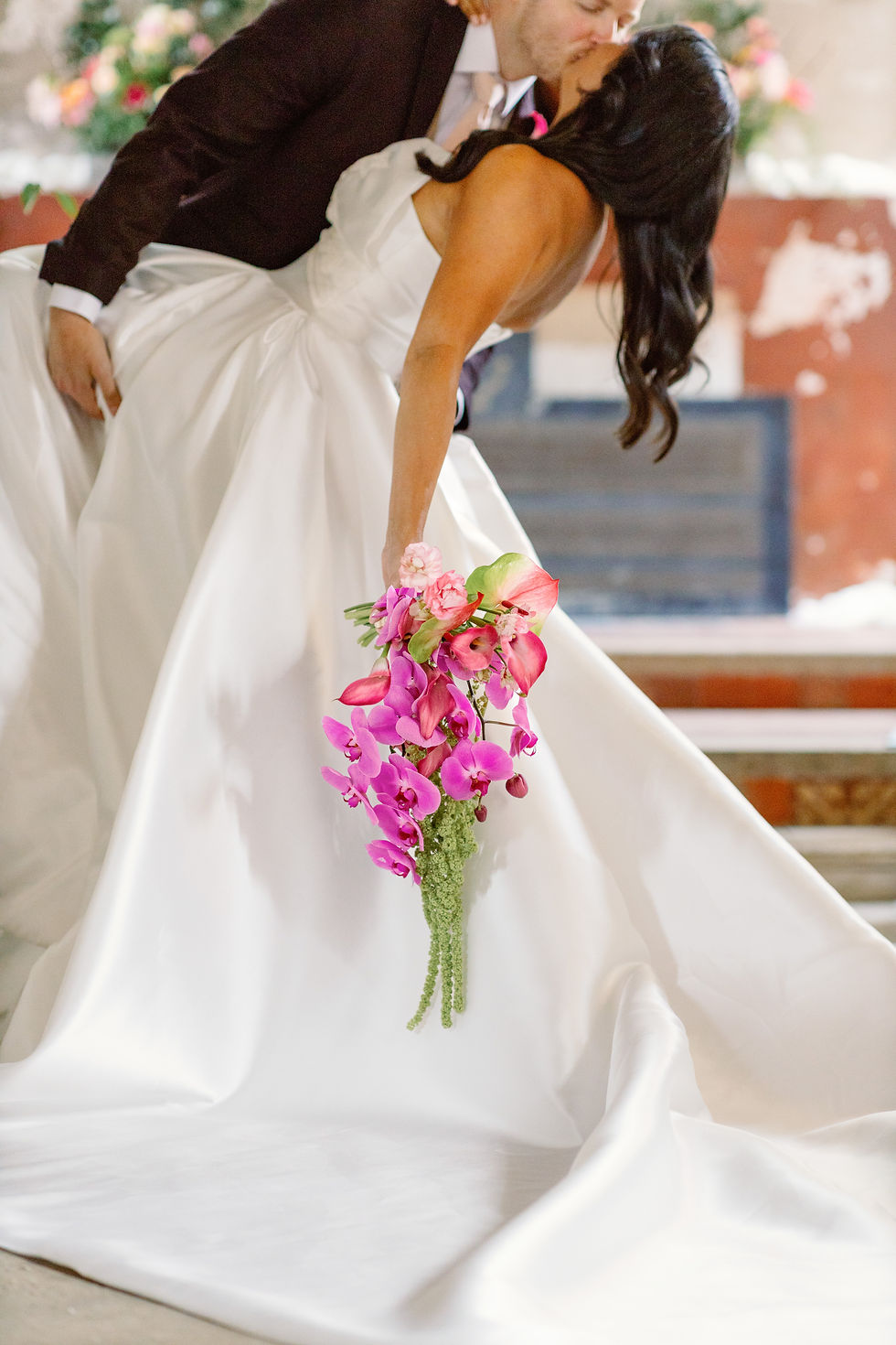 Bride in white gown and groom kiss during wedding dip in the bell tower at the Elevtham Hotel, holding a bright pink orchid bouquet in a soft, romantic indoor setting