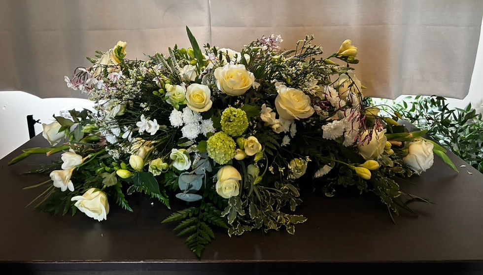 Large white and cream floral arrangement of roses and greenery on a dark table, with a soft, elegant mood. Funeral flowers in Alton hampshire