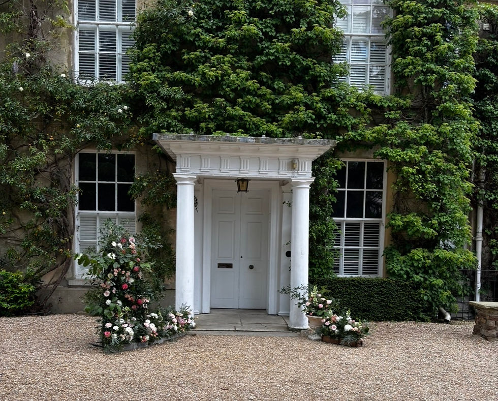 Ivy-covered northbrook park entrance with white columns, white door, and pink-and-white flowers beside a gravel courtyard.