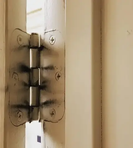 Close-up of black soot and smoke residue on a door hinge, demonstrating the need for professional fire damage restoration Utah and deep cleaning.