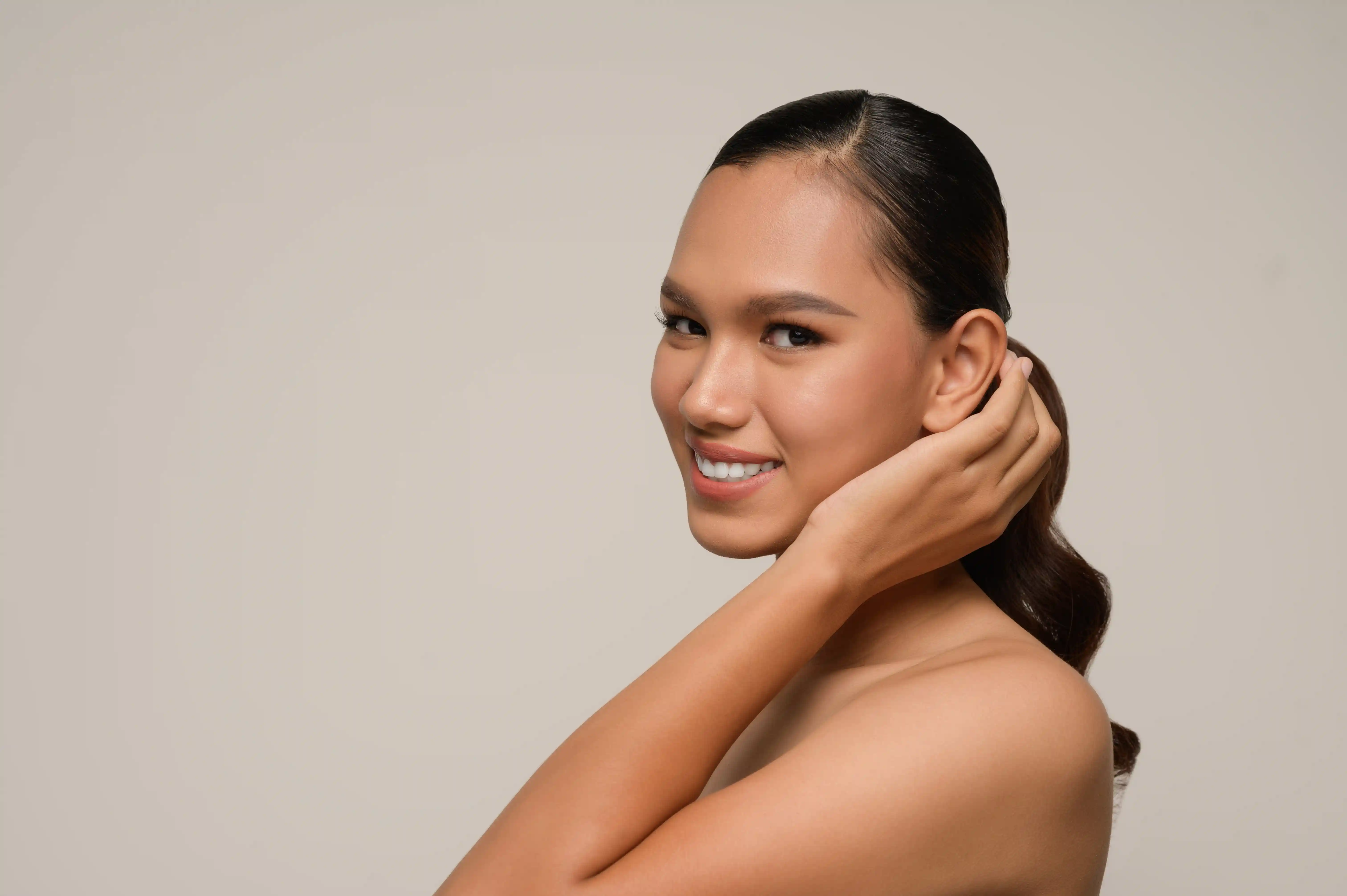 A woman smiling while putting her hair behind her ears showing her otoplasty results