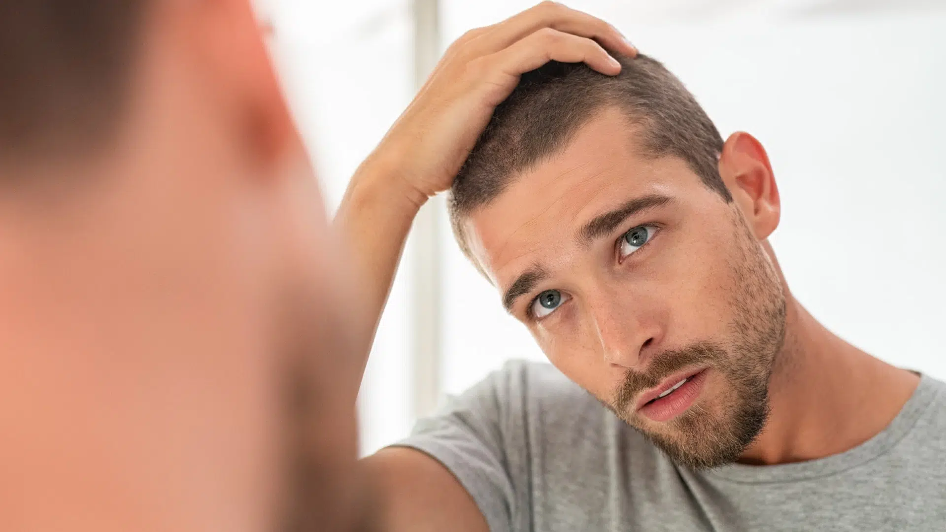 A man looking at himself on a mirror checking his hair growth after hair transplant