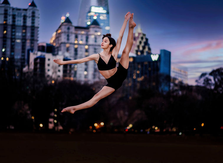 Ballerina performing a high tilt jump at night with Atlanta skyline glowing behind her during dance session