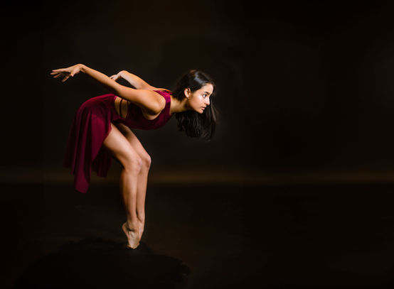A ballerina performing sharp, precise moves against a dark studio background, capturing the power and focus of her elegant movement.