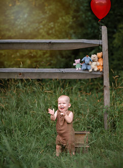 Atlanta baby photography of a one-year-old boy stands in front of a Winnie the Pooh-themed fence, opening his hands in joy, radiating excitement and happiness.