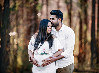 Pregnant woman in an embrace with her partner, who is kissing her on the temple.