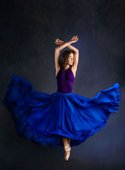A ballerina en pointe in a flowing blue skirt stands against a dark background