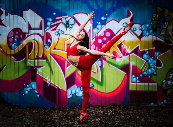A ballerina in a red outfit poses against a graffiti-covered wall in Atlanta, combining the energy of street art with the elegance of dance.
