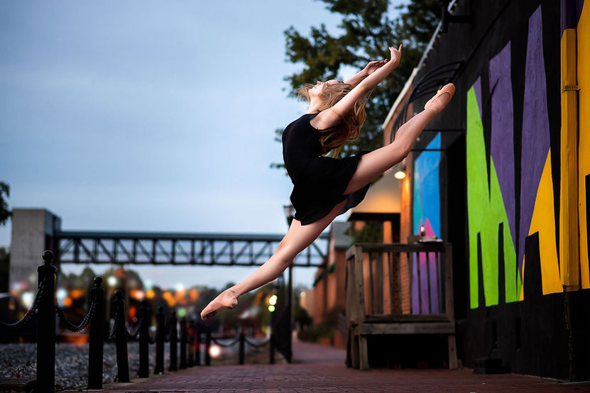 A dancer performs a firebird jump in front of a colorful urban mural