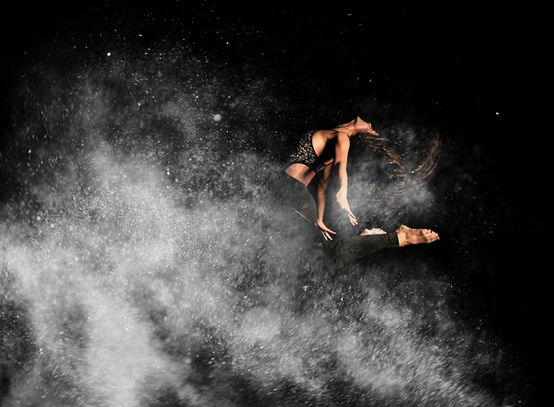 A dancer leaps mid-air with chalk powder surrounding her, capturing a moment of motion and energy as the powder swirls around her form.