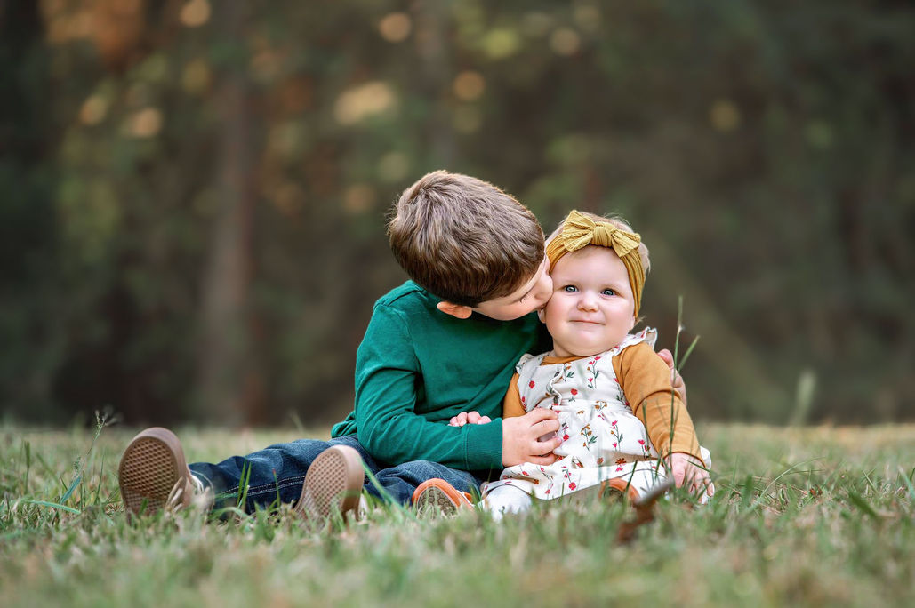 Little siblings sharing a sweet moment sitting on grass