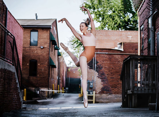 A joyful dancer mid-air in a brick alley in Marietta Square, radiating energy and grace against the raw urban backdrop.