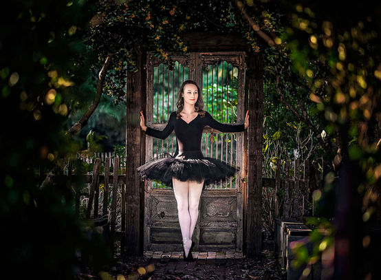 Atlanta dancer ballerina in a black tutu stands en pointe in a garden in Atlanta, her graceful form set against the vibrant greenery.