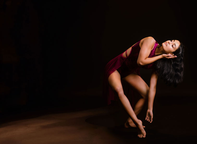 A ballerina in a dark red outfit dances against a dark background