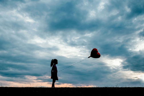 silhouette of a little girl holding a ballon against beautiful sunset