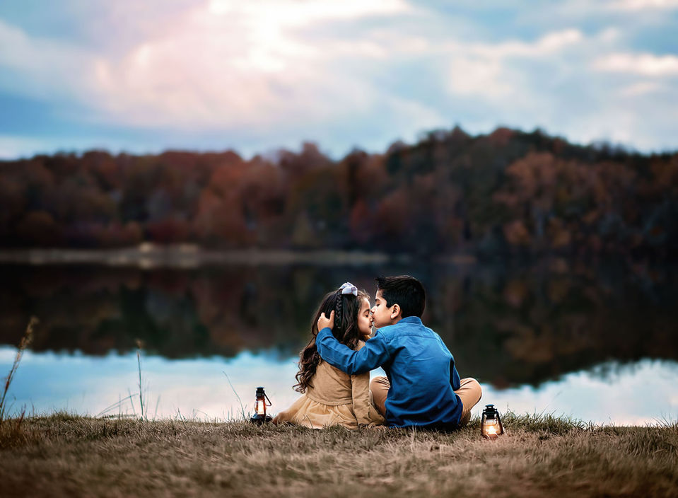 Siblings sitting on the edge of a lake during a beautiful sunset