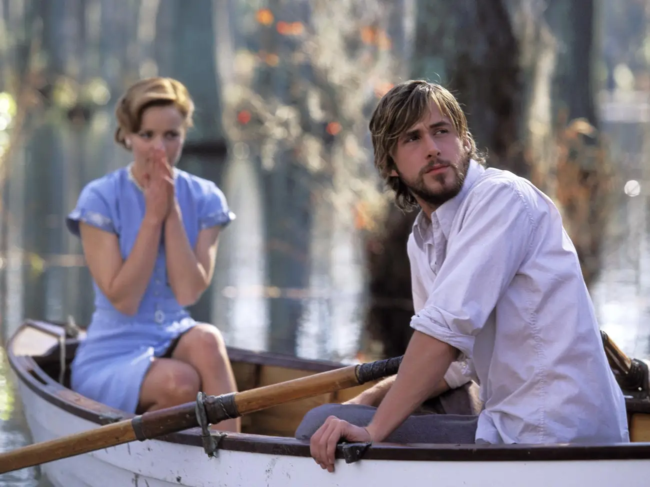 Allie and Noah from "The Notebook" sitting in a boat on a river, with Allie covering her mouth and Noah looking away contemplatively.