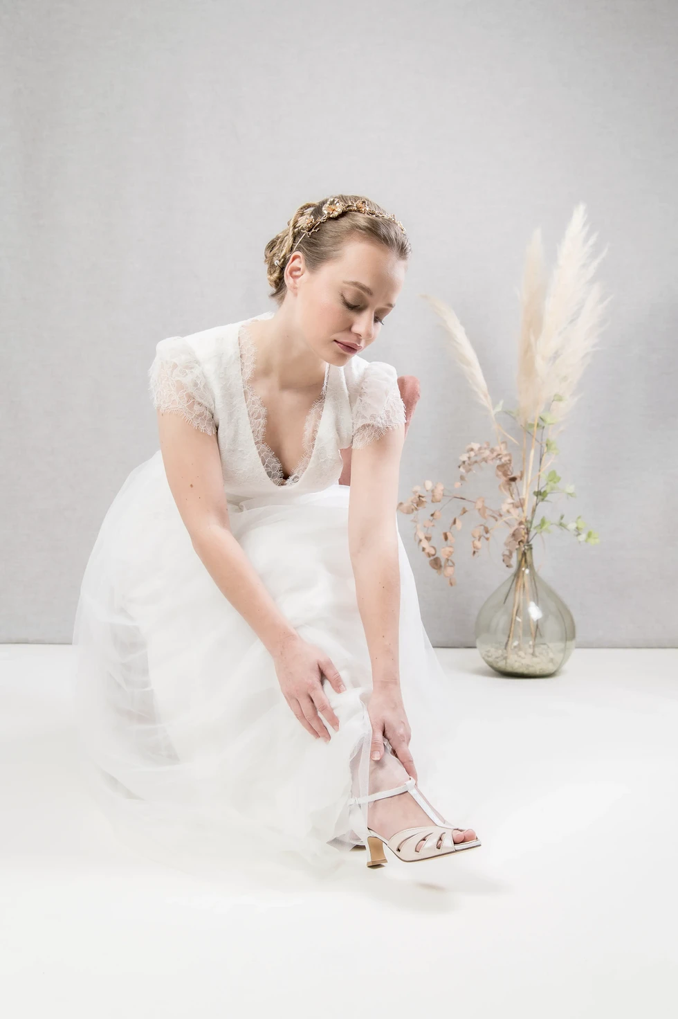 Mariée en robe blanche ajustant sa sandale – détail élégant mis en scène par Fred Photo, photographe mariage et mode.