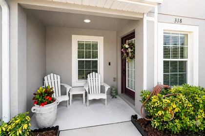 Front porch with two chairs, small table, potted plants, and covered entryway with landscaped greenery.