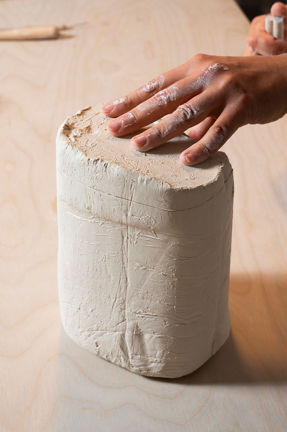 Hands lifting a cleanly sliced section of porcelain, ready for rolling.
