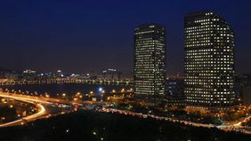 vista nocturna urbana con dos rascacielos iluminados, río al fondo y estelas de autos en una autopista tecnología lg