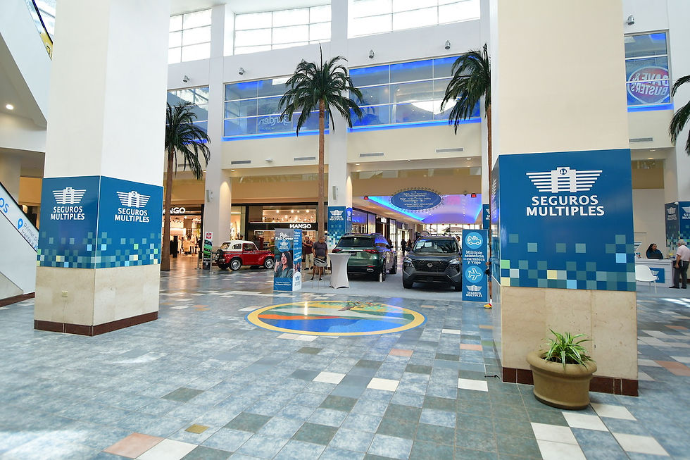 PRIAS centro comercial en plaza de las américas luminoso con autos expuestos, letreros azules de Seguros Múltiples y tienda Mango al fondo.