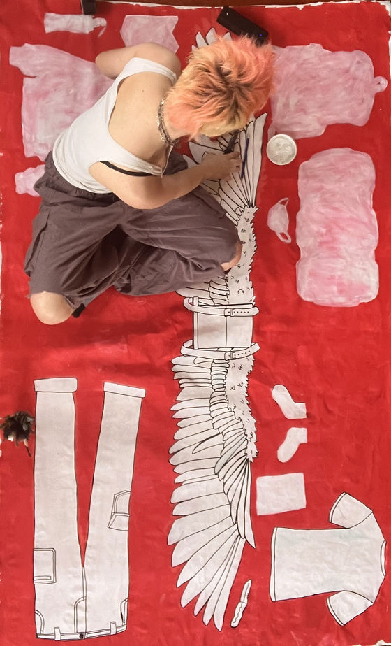 Person with pink hair, white tanktop, and baggy pants sitting on a red and white painting.