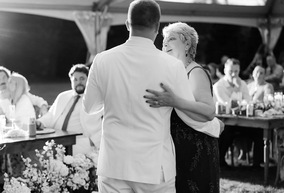 Mother son dance at tented wedding reception with guests watching