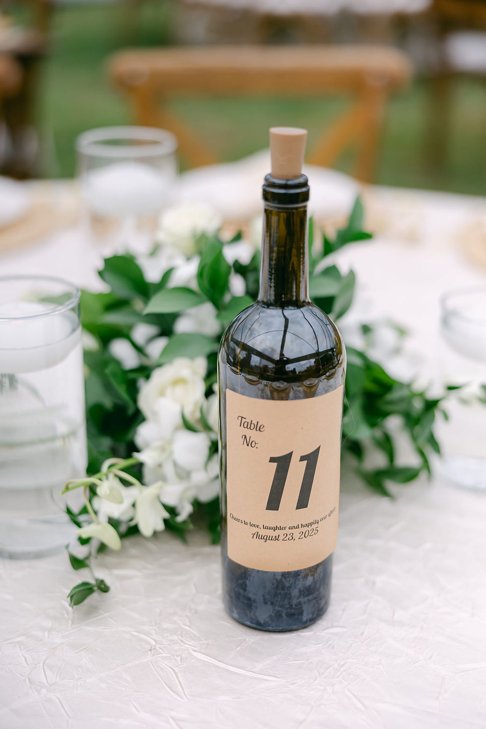 Wedding table numbers displayed on wine bottles at outdoor reception