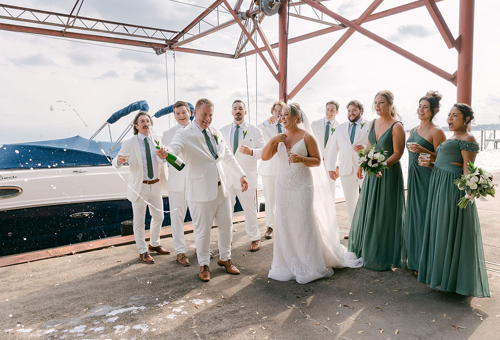 Bride and groom celebrating with champagne pop by the water with bridal party