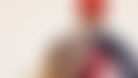 Worker in plaid shirt and red hard hat draped in an American flag, facing a bright, neutral background. Mood is patriotic.