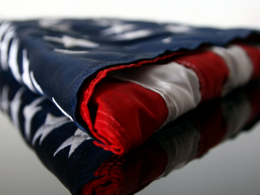 Folded American flag on reflective surface with visible stars and stripes, featuring red, white, and blue colors. Quiet, respectful mood.